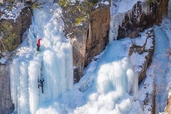 a waterfall with trees on the side of a snow covered slope