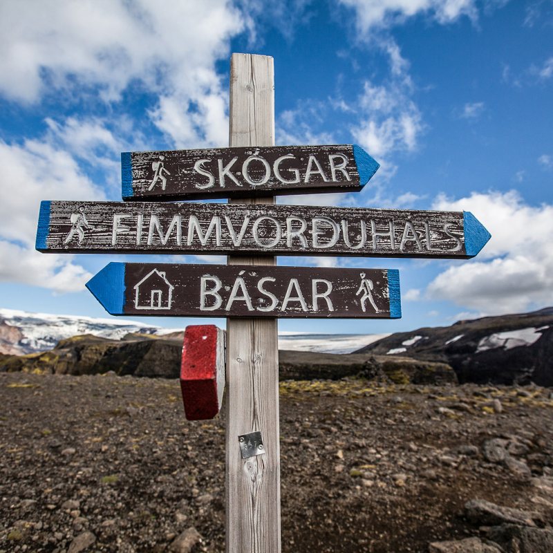 Wooden signpost on rocky terrain with blue sky, pointing to hiking trails.